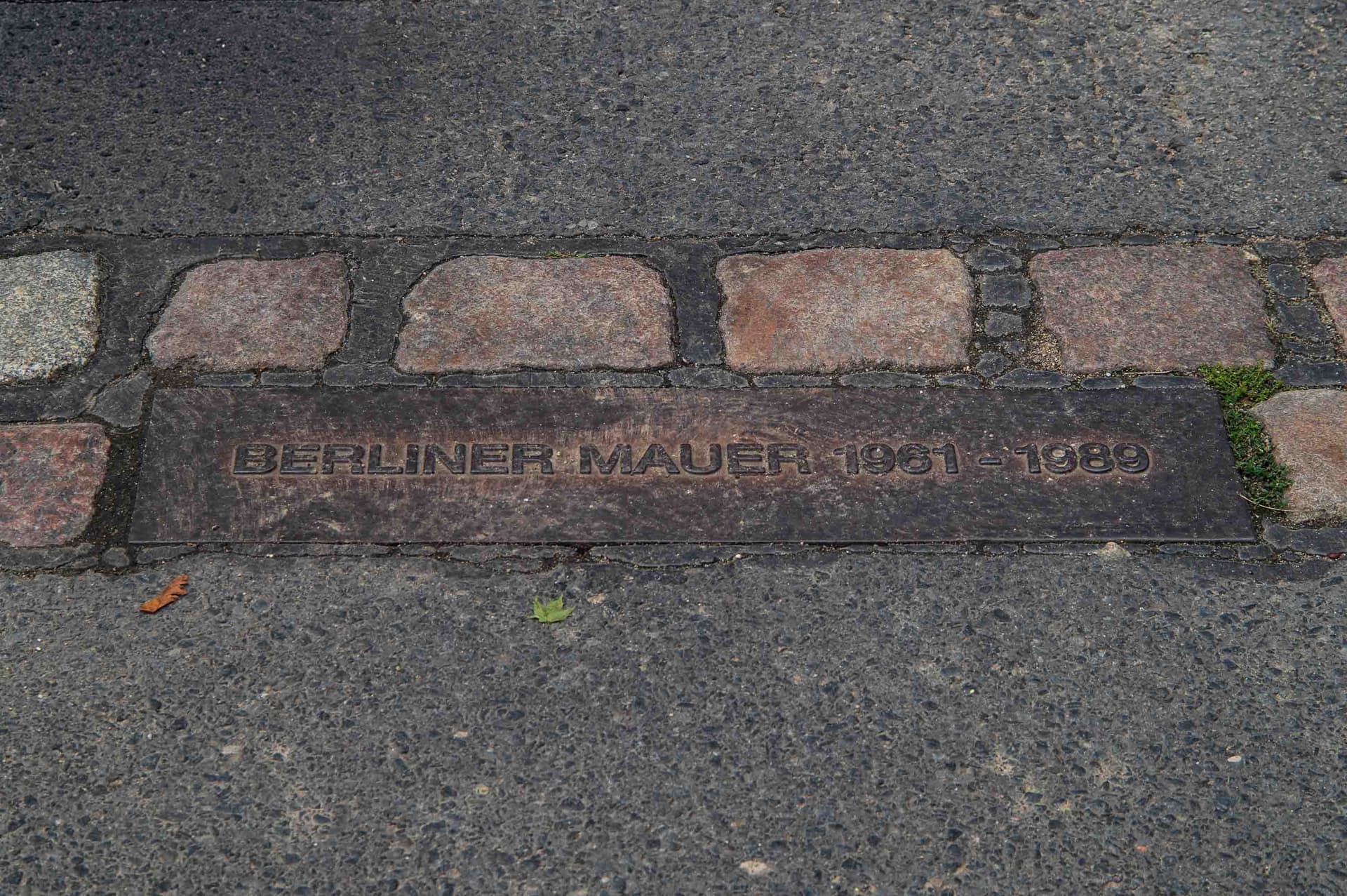 A plaque set in the asphalt marks the Wall's exact path: "Berliner Mauer 1961-1989."