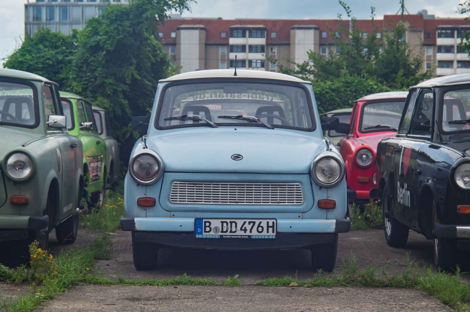 A pale blue Trabant, head-on, among its colorful siblings.